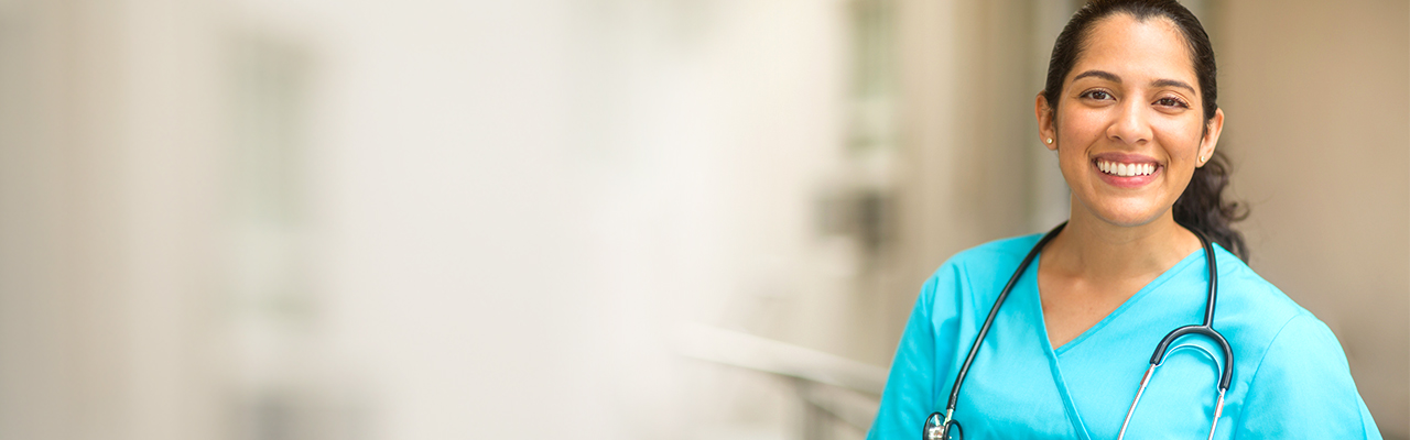 Smiling female healthcare professional looks at the camera while in hospital hallway.