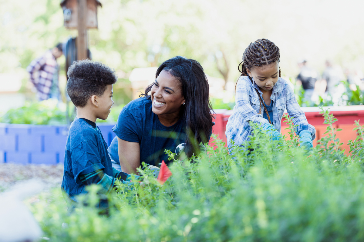 Woman smiling at young boy with young girl in a garden.