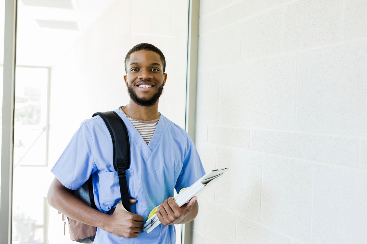 Male student smiling carrying a backpack and notebook heading to class