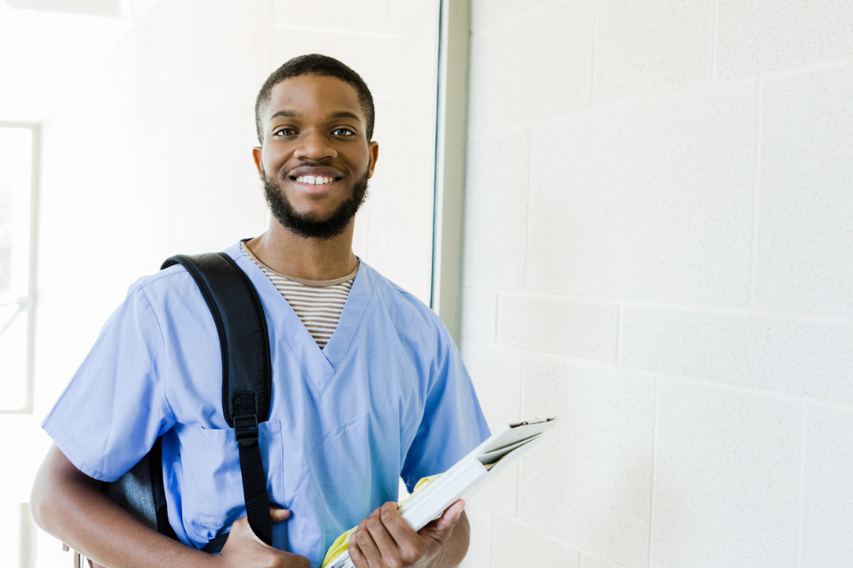 Male student smiling carrying a backpack and notebook heading to class