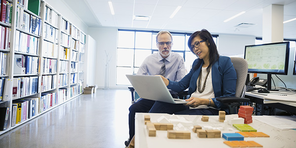 Two professionals looking at a laptop in an office setting.